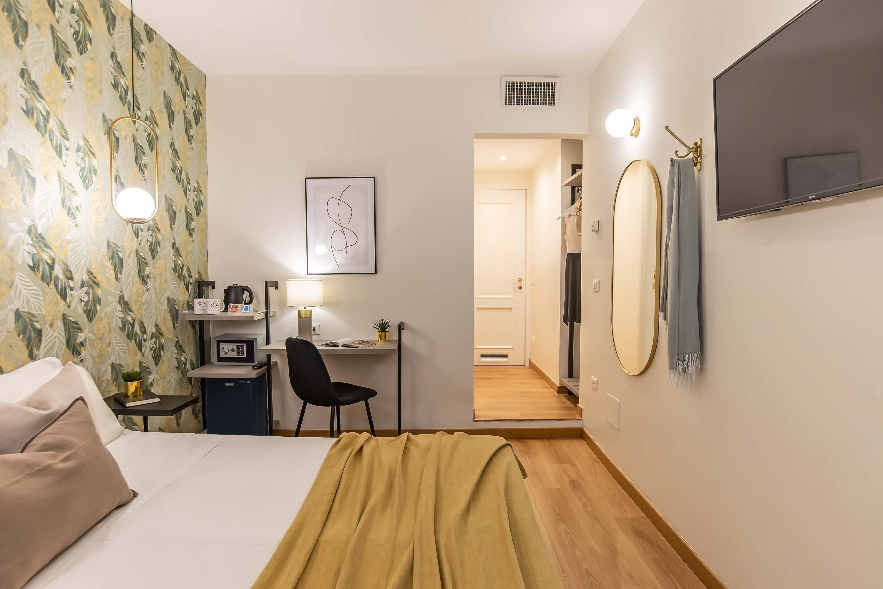A hotel room with a bed, desk, chair, and a mirror.