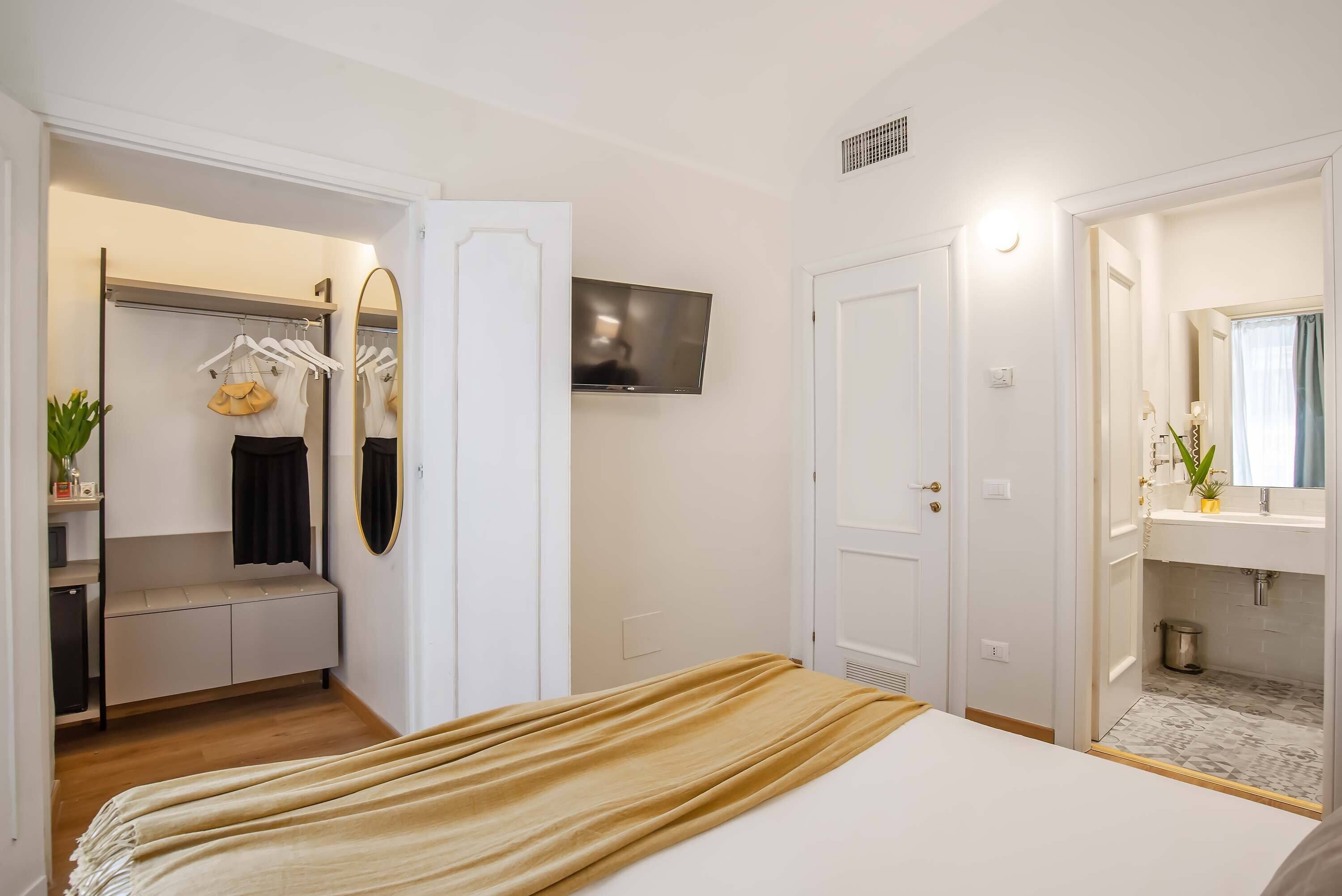 Un dormitori amb un llit, un armari, una televisió i un bany amb un lavabo i mirall.