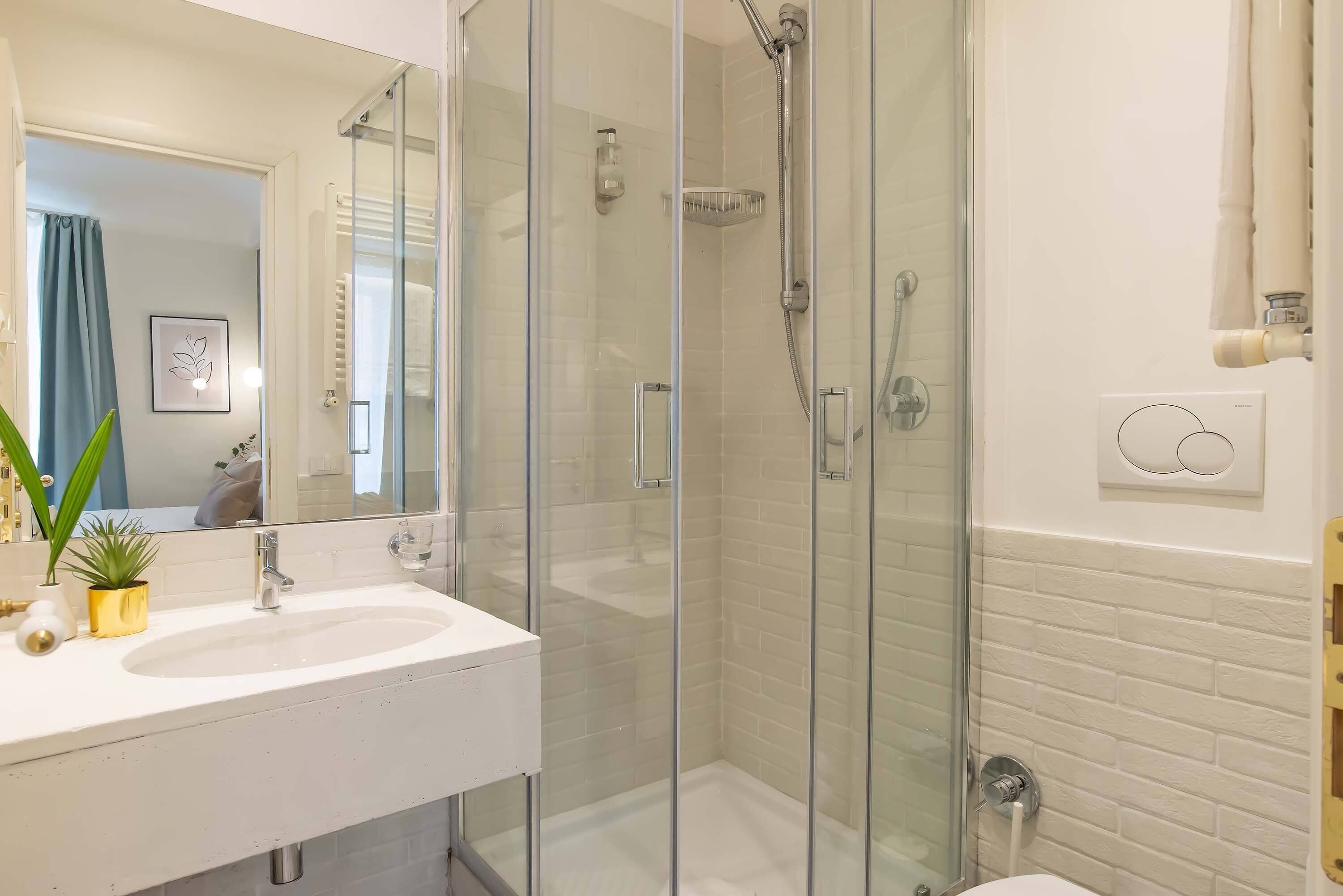 Un baño moderno con cabina de ducha de vidrio, un lavabo blanco y un espejo sobre él.