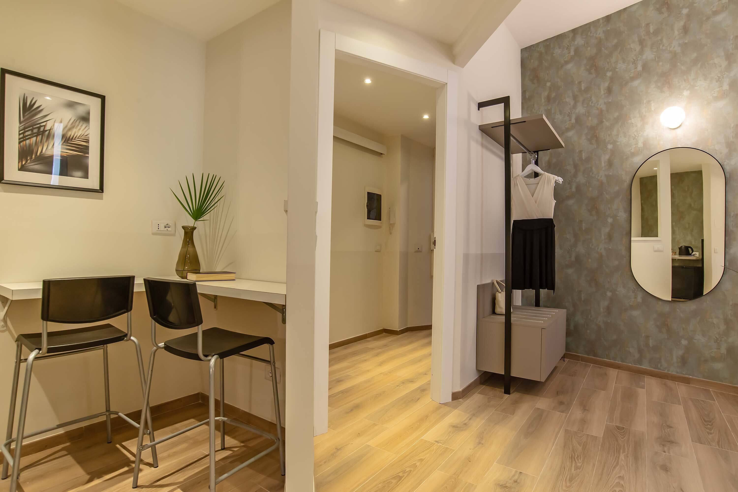 A modern hotel room with a wooden floor, a desk with two chairs, a mirror, and a plant.