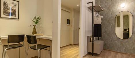 A modern hotel room with a wooden floor, a desk with two chairs, a mirror, and a plant.