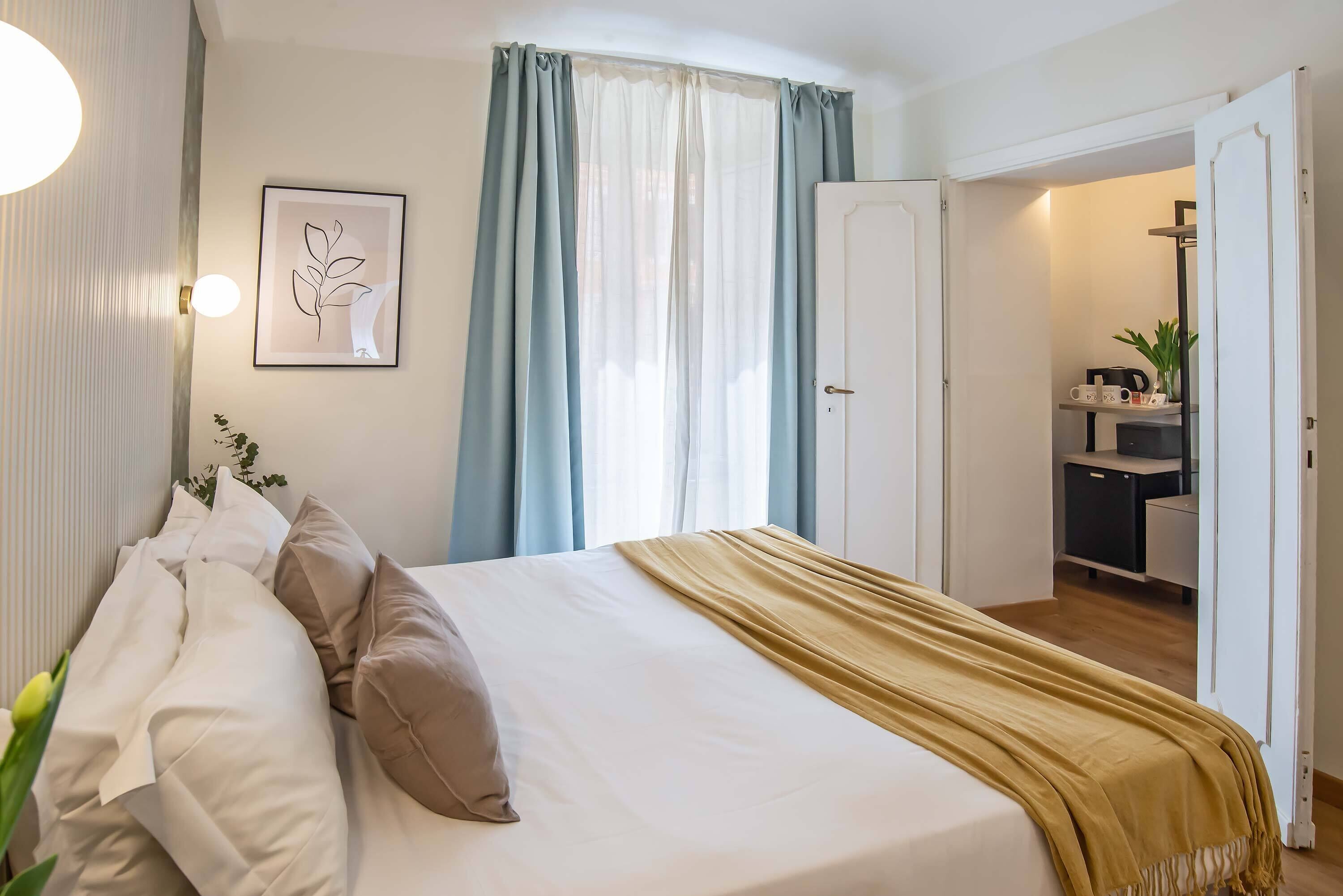 A neatly made bed with a white and beige duvet, a gold throw blanket, and a framed artwork on the wall.