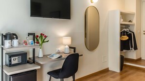 Hotelkamer met flatscreen televisie, bureau met lamp, stoel, kluisje, kleine koelkast, spiegel en kast met hangende kleding.