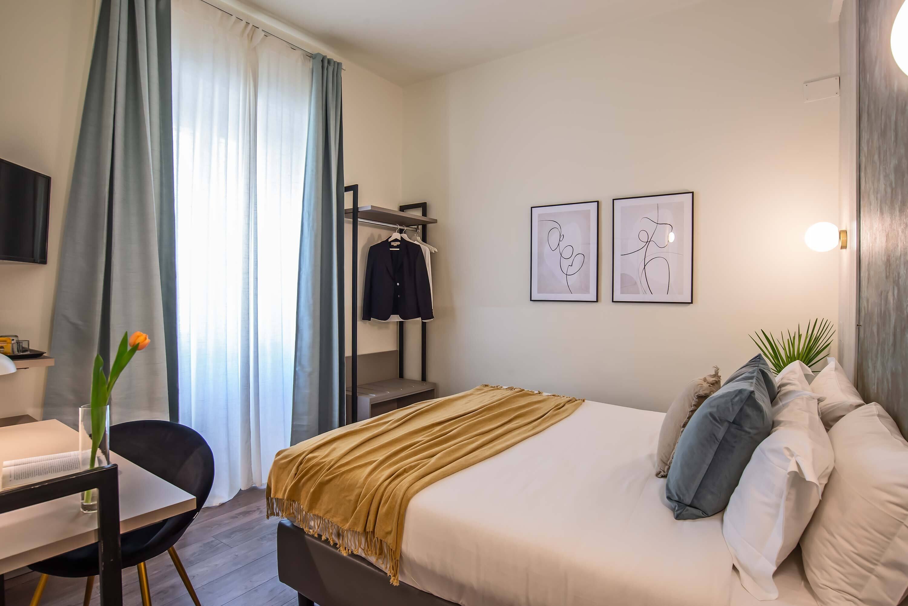 Une chambre d’hôtel équipée d’un lit, d’un bureau, d’une chaise, d’une télévision et d’une fenêtre avec des rideaux.