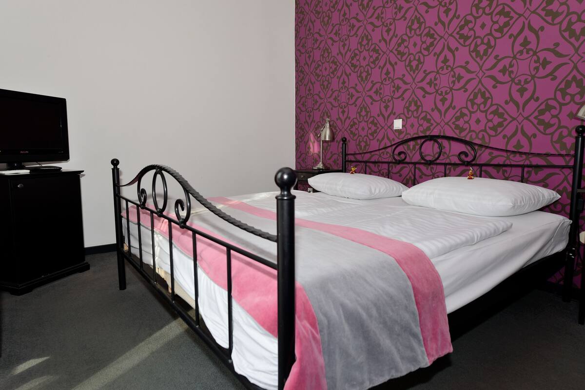 A single bed with a metal frame, a bedside table, and a television on a dresser.