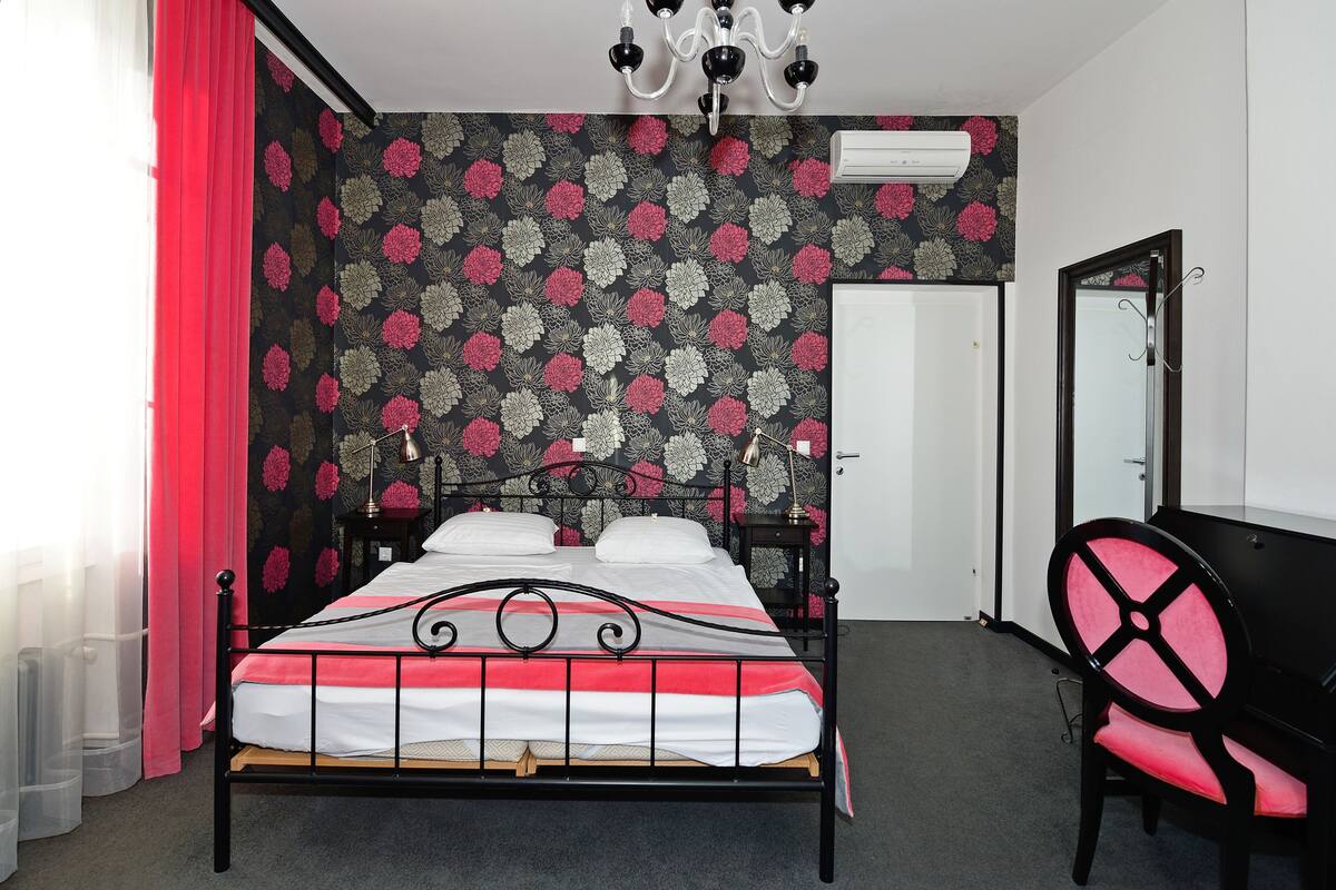 A neatly arranged bedroom with a bed, bedside table, lamp, and a mirror.