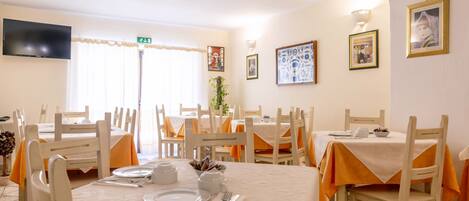 A dining area with tables set for four, white chairs, and orange tablecloths.