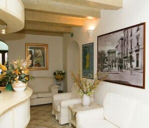 Um quarto com um sofá branco, uma mesa pequena e uma fotografia a preto e branco emoldurada na parede.
