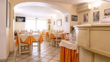 Un comedor con mesas preparadas para comidas, una barra de cocina y un televisor montado en la pared.