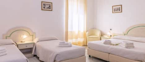 A hotel room with three beds, a sitting area, and a window with curtains.