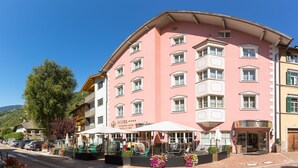 Ein mehrstöckiges Hotel mit rosafarbenem Fassadengestalt, einer Außenbestuhlung und einem gut sichtbaren Eingang.