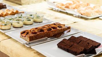 Una mesa de postres con diversas opciones horneadas, incluyendo una porción de pastel con fruta, brownies y pequeños postres en vasos.