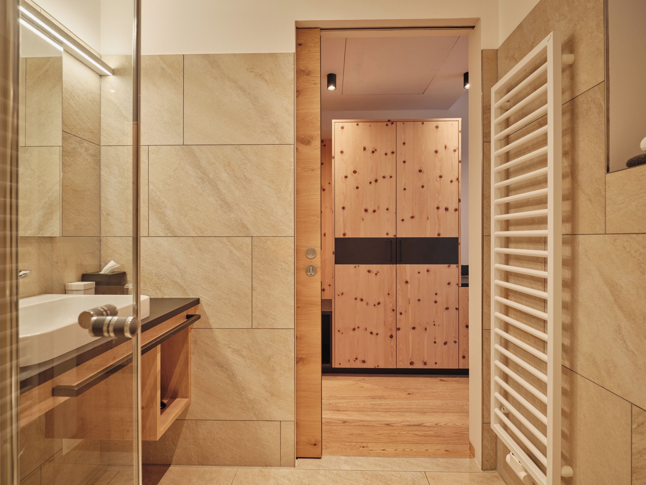 Un baño moderno con cabina de ducha de vidrio, tocador de madera y un vestidor con puerta de madera.