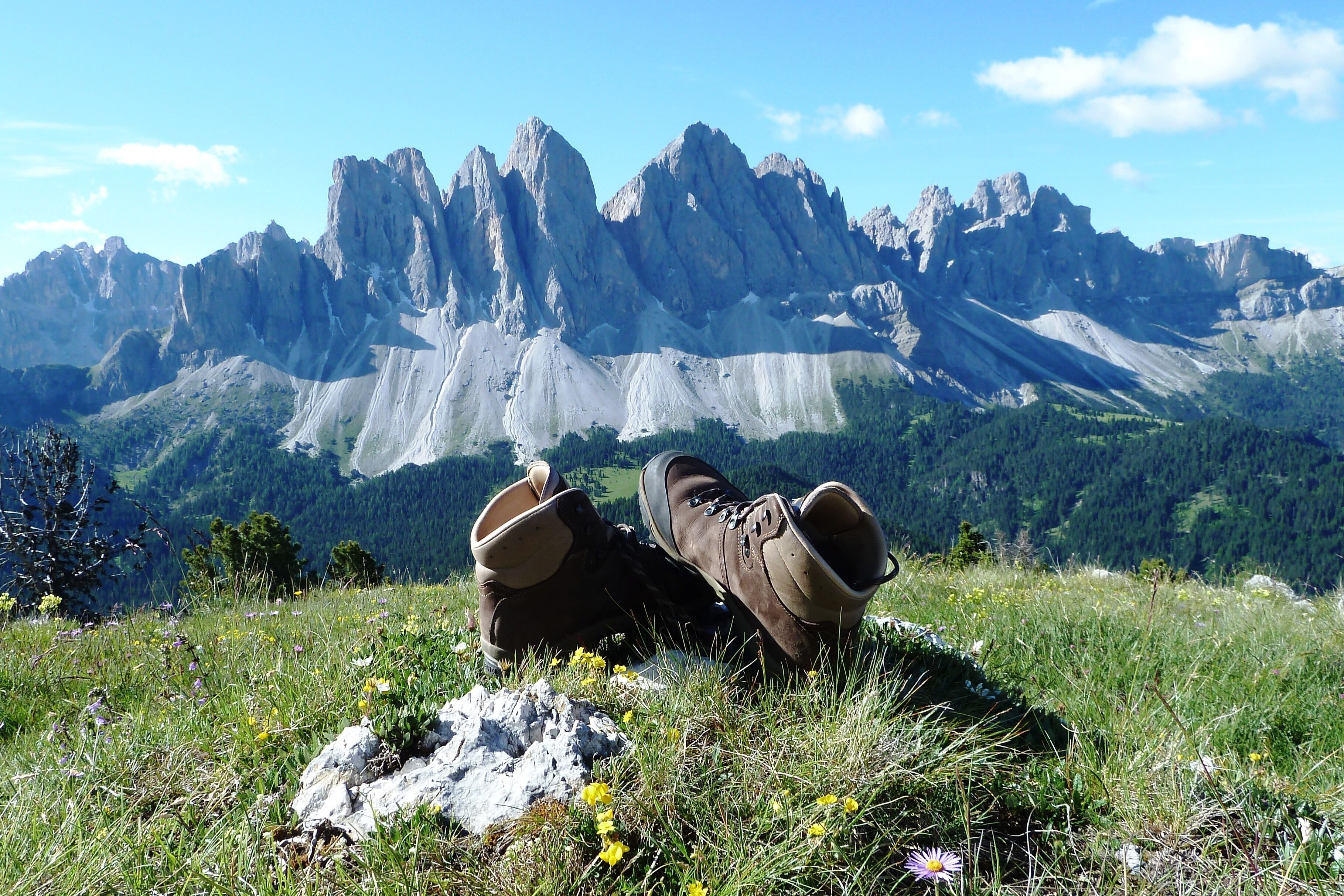 A pair of boots on a grassy hill with a mountain range in the background.
