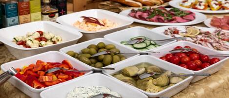 A buffet with various food options including olives, cherry tomatoes, and a creamy dip.