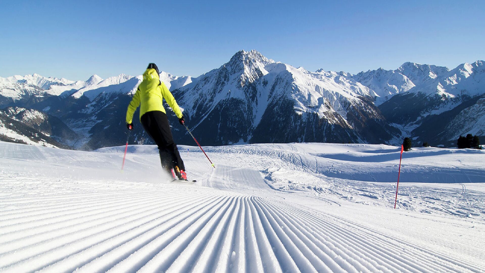 A person skiing on a groomed slope with a mountainous backdrop.