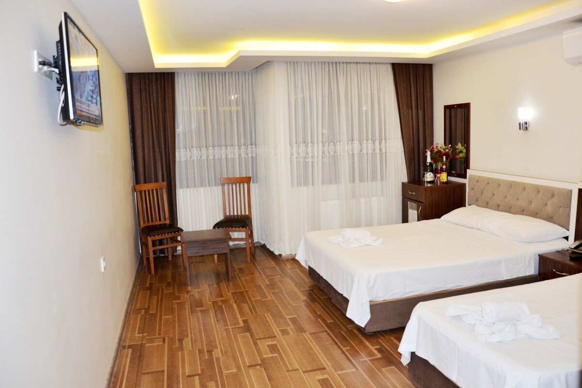 Habitación de hotel con dos camas, una silla de madera, una mesita pequeña y un televisor montado en la pared.