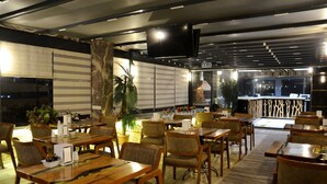 Un restaurante con mesas y sillas de madera, una planta grande y un televisor montado en el techo.