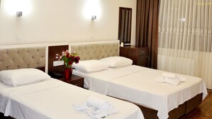 Una habitación de hotel con dos camas, una mesita de noche con un florero y un espejo, además de una ventana con cortinas.