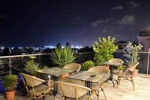 An outdoor seating area with tables and chairs, surrounded by potted plants, overlooking a cityscape at night. - Grand Mark Hotel (Istanbul)
