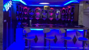 Zona de bar con luces de neón, taburetes y estantes llenos de botellas.