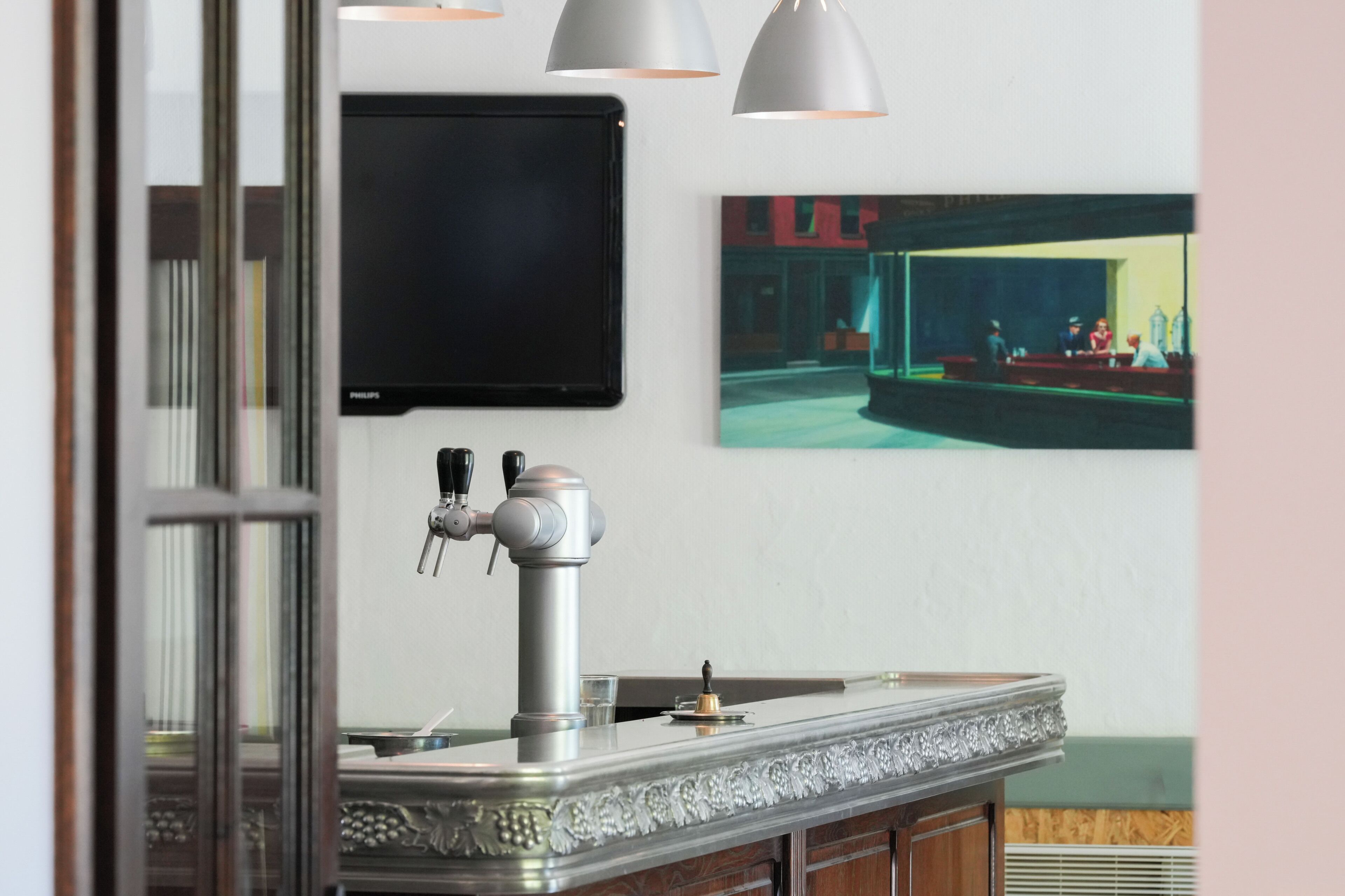 Angolo bar con un rubinetto, un'opera d'arte incorniciata e una televisione a parete.