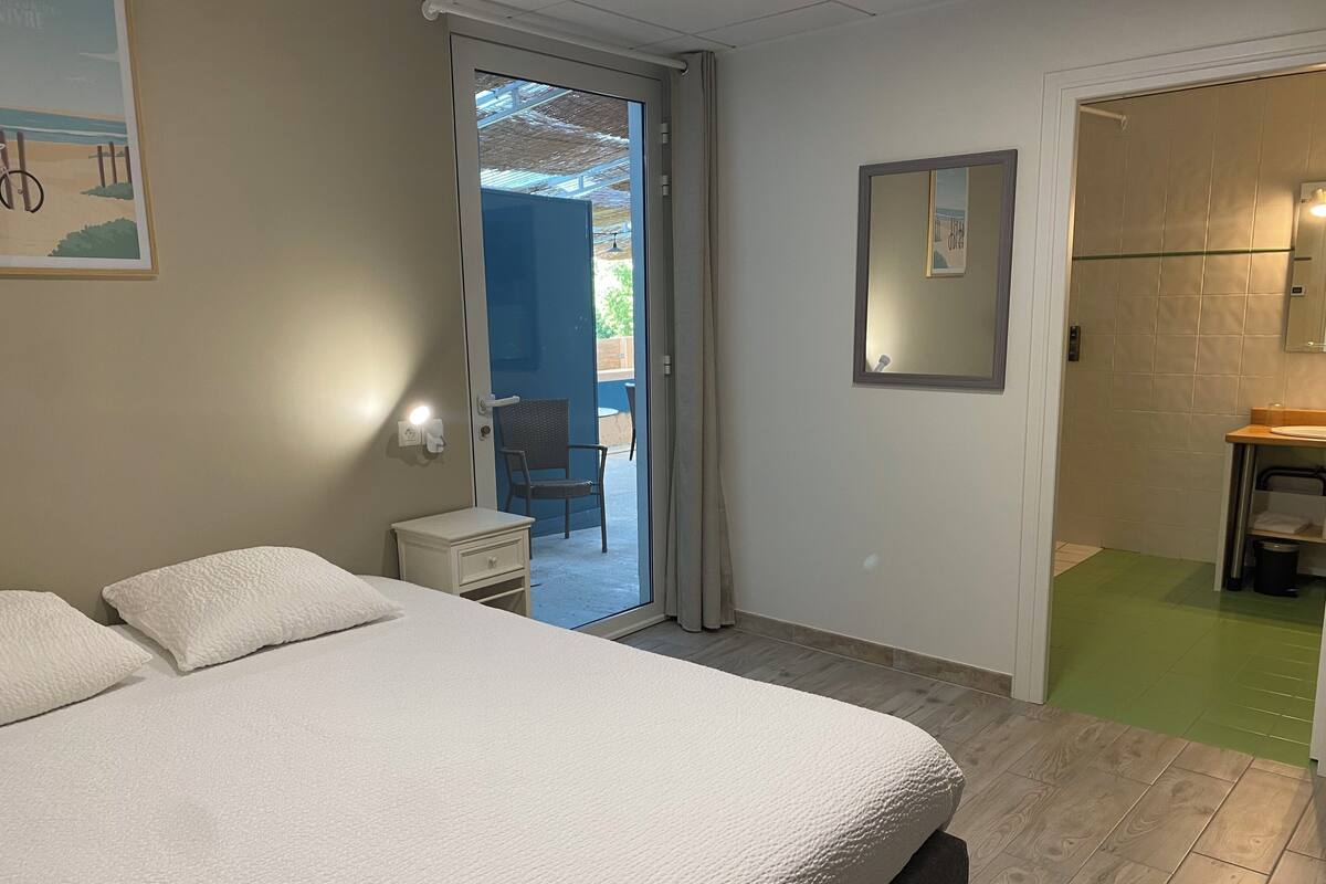 A bedroom with a bed, a nightstand, a chair, and a bathroom visible through an open door.