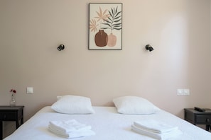 Ein Hotelzimmer mit einem Bett, weißen Kissen, einem gerahmten Kunstwerk über dem Bett, zwei Nachttischen und einem Beistelltisch mit einer Fernbedienung.