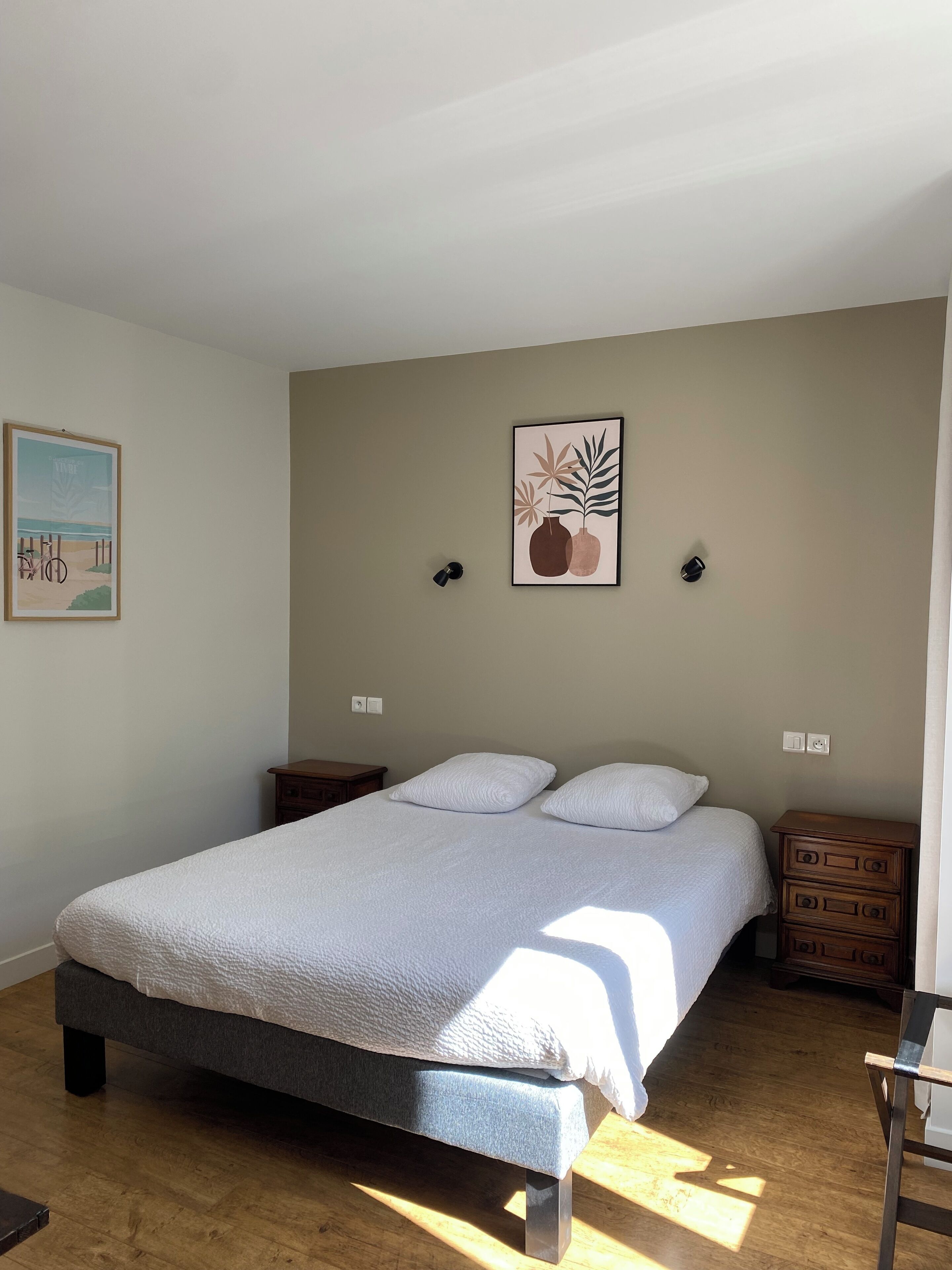 A bedroom with a bed, two bedside tables, a nightstand, a dresser, and two wall-mounted lamps.