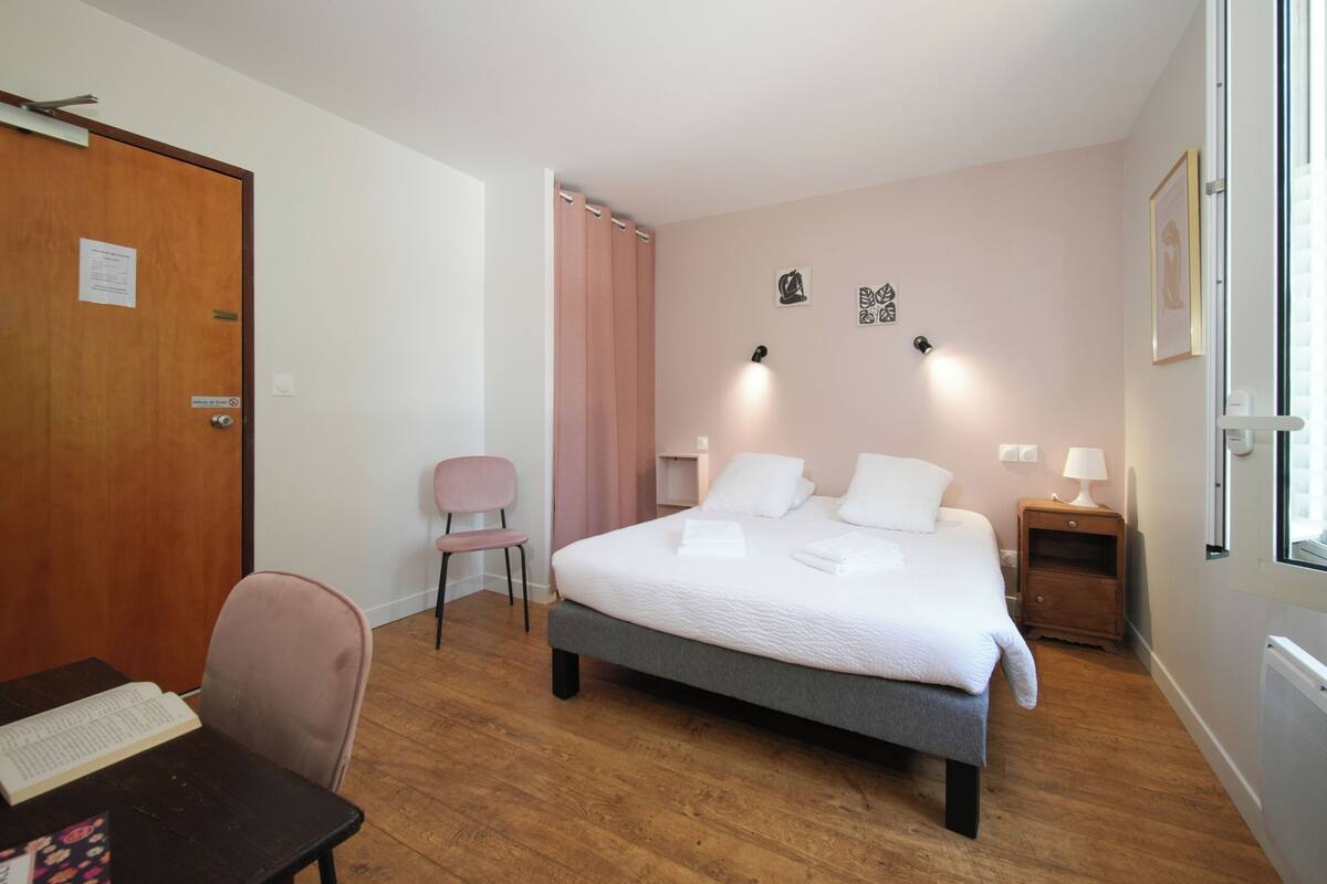 A bedroom with a bed, a desk, a chair, a nightstand, and a door.