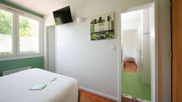 A bedroom with a bed, a TV mounted on the wall, a painting, and a view of a green-tiled hallway.