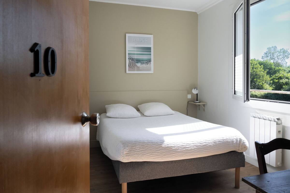 A bedroom with a bed, a door with the number 10, a bedside table, a window, and a radiator.