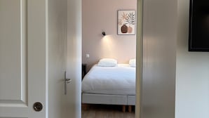 Ein schmaler Flur, der in ein Schlafzimmer führt, mit einem Bett, einer Wandleuchte und einem gerahmten Bild.