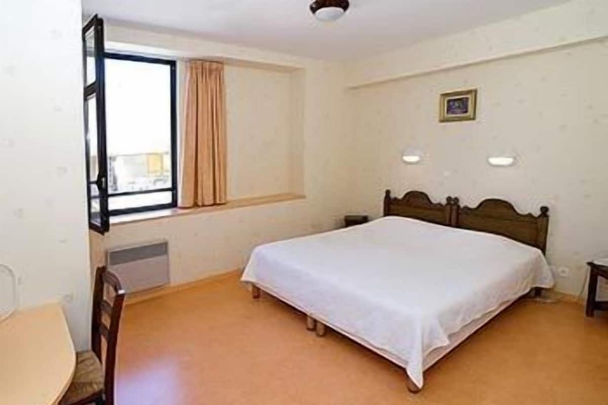 A bedroom with a single bed, a window with curtains, a bedside table, and a chair.