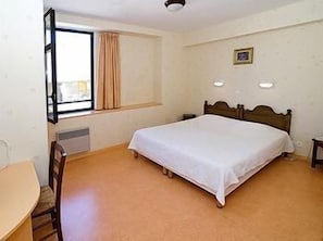 Quarto com uma cama de solteiro, janela com cortinas, mesa de cabeceira e uma cadeira.