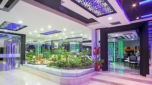 A modern hotel lobby with a central garden, glass partitions, and contemporary lighting fixtures. - Tanjah Flandria (Tangier)