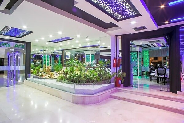 A modern hotel lobby with a central garden, glass partitions, and contemporary lighting fixtures. - Tanjah Flandria (Tangier)