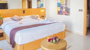 A hotel room with a large bed, a bedside table, a round wooden table with fruit, and a TV on the wall. - Tanjah Flandria (Tangier)