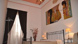 A bedroom with a bed, a nightstand, a lamp, a painting, and a window with curtains. - San Giovanni in Laterano (Rome)