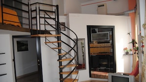 A modern interior with a spiral staircase, a flat-screen TV, and a kitchen area. - San Giovanni in Laterano (Rome)