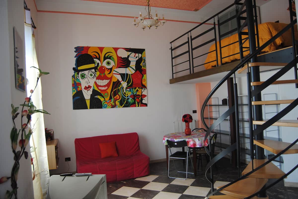A room with a red sofa, a dining table with chairs, a colorful abstract painting, and a spiral staircase.