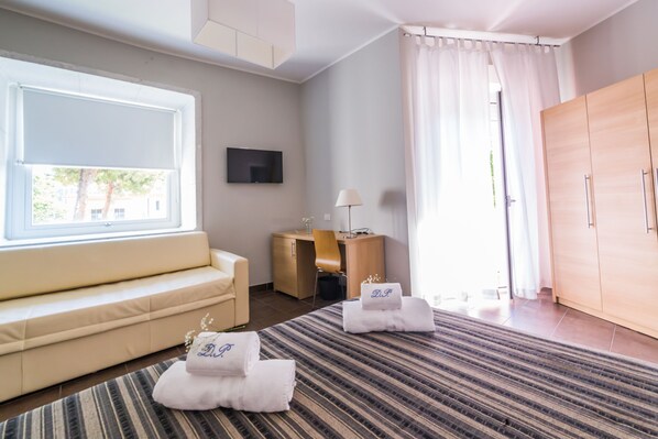 A hotel room with a sofa, a desk, a TV, a wardrobe, and two towels with initials on them. - Du Parc Hotel (Gabicce Mare)