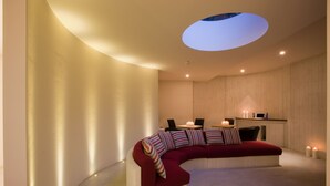 Un sofá moderno y curvo con un cojín rojo y almohadas a rayas en una habitación luminosa con tragaluces.
