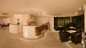 Un moderno vestíbulo de hotel con mostrador de recepción, zona de estar y una escalera que conduce a otro piso.