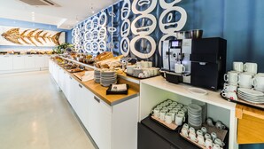 Un moderno comedor para el desayuno con una barra alargada, máquinas de café y una variedad de alimentos para el desayuno.