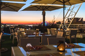 An outdoor dining area with tables and chairs, umbrellas, and a view of the sunset over the water. - Du Parc Hotel (Gabicce Mare)