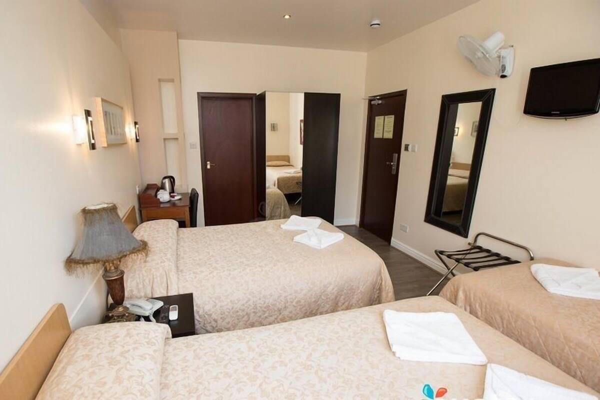 A hotel room with two beds, a desk, a lamp, a TV, and a mirror.
