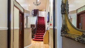 A grand hallway with a red carpeted staircase, ornate wall decorations, and a large mirror. - Notting Hill Gate Hotel (London)