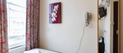 Habitación de hotel con una cama, teléfono, espejo y ventana con cortinas.