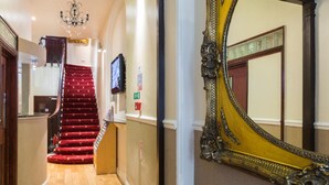 A grand staircase with red carpet, a large ornate mirror, and a chandelier. - Notting Hill Gate Hotel (London)